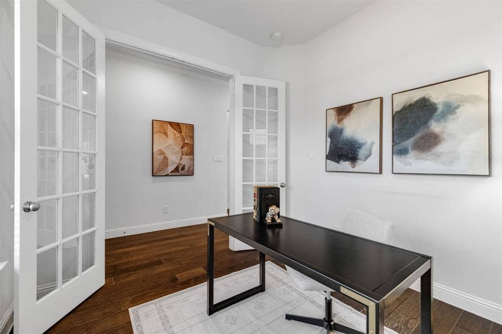 Sophisticated home office featuring gleaming wood-finish flooring, white French doors with multi-pane glass panels, and a black metal-frame desk