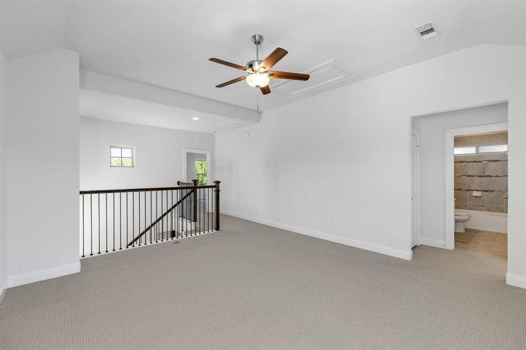 Carpeted loft area with a ceiling fan, wrought iron and wood railing, and a window