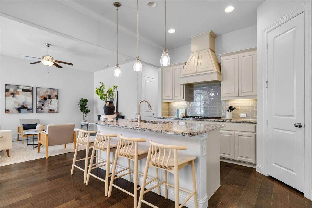Kitchen island with a granite countertop, white cabinetry, decorative range hood, subway tile backsplash, and wood-finish flooring