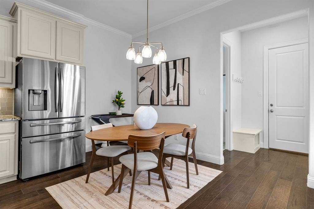 Stainless steel refrigerator, upper cream cabinetry, subway tile backsplash, wood-finish flooring, and a modern chandelier
