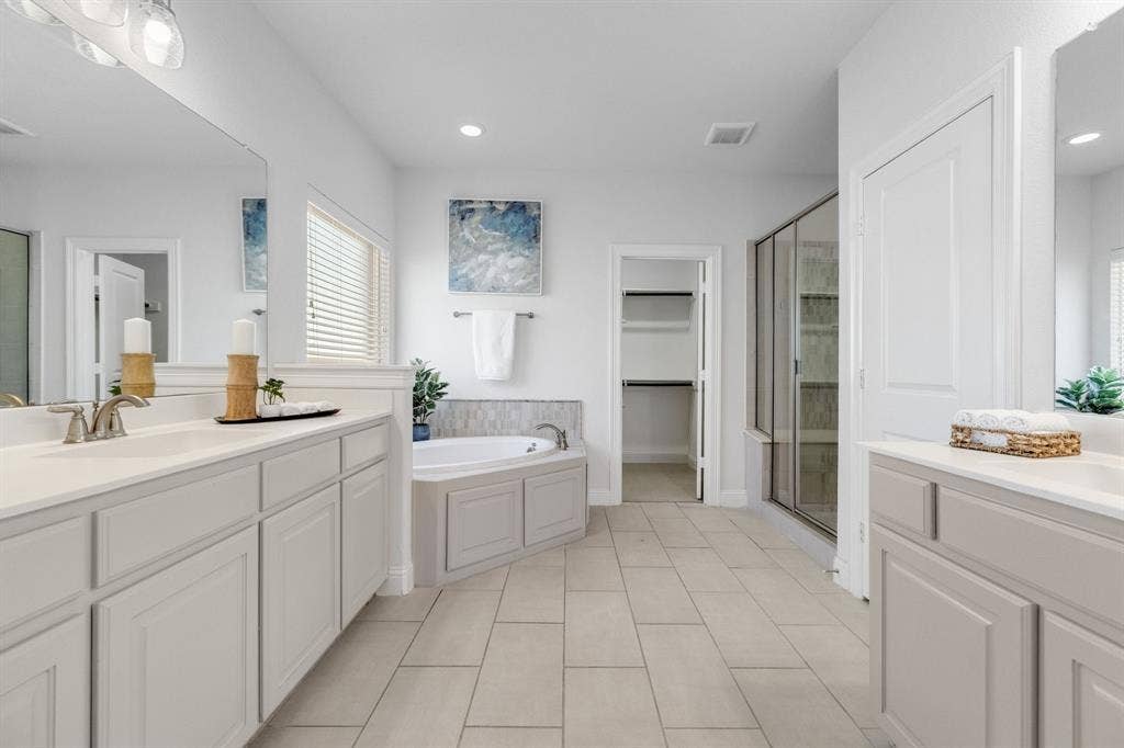 Dual vanity with white countertops, built-in soaking tub, glass-enclosed shower, walk-in closet, and tiled flooring