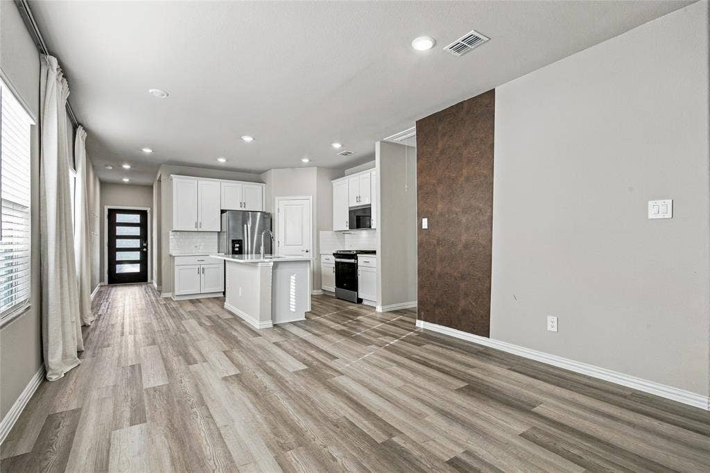 113 Greenbriar Drive, Princeton, TX 75071 Wood-finish flooring throughout, recessed ceiling lighting, kitchen island with built-in sink, white cabinetry with integrated appliances, and a modern entry door