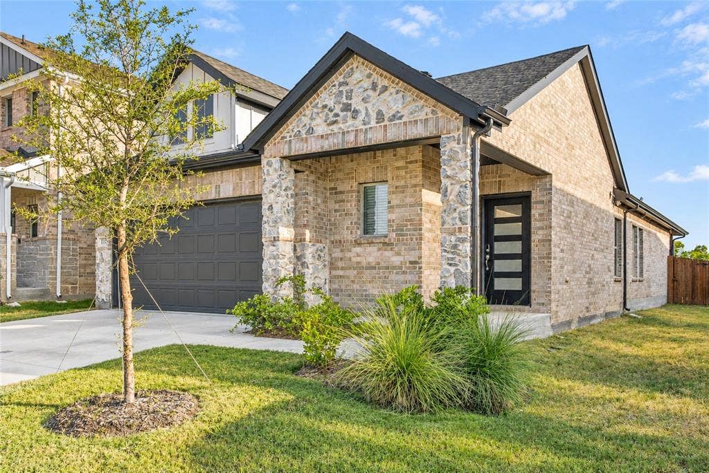 113 Greenbriar Drive, Princeton, TX 75071 Brick and stone facade, dark-framed entry door with frosted glass panels, attached two-car garage, established front landscaping, and a concrete driveway
