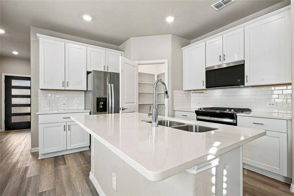 113 Greenbriar Drive, Princeton, TX 75071 Kitchen featuring white cabinetry, stainless steel appliances, a center island with double sink, and wood-finish flooring