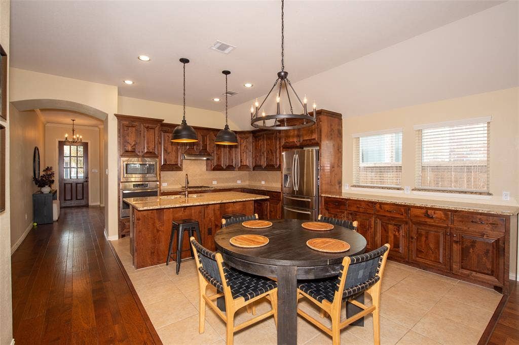 Kitchen with wood-finish cabinetry, stainless steel appliances, a center island with sink, and tile flooring