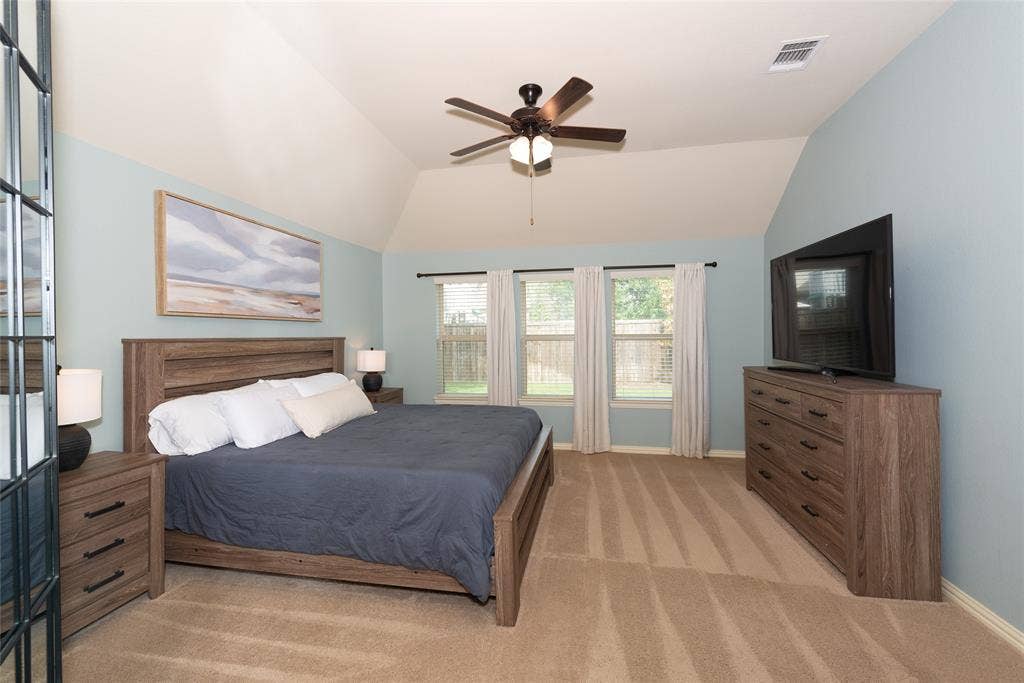 Vaulted ceiling, three windows, ceiling fan, wood-finish flooring, and light blue wall color