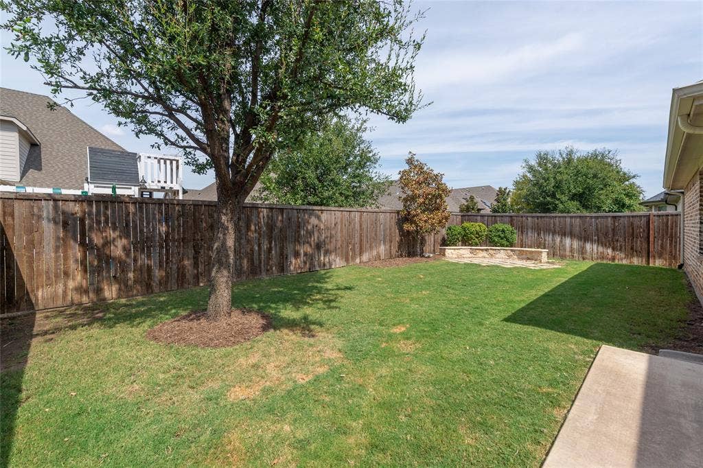 Expansive backyard with a manicured lawn, established tree, wood privacy fence, and stone-finished planter