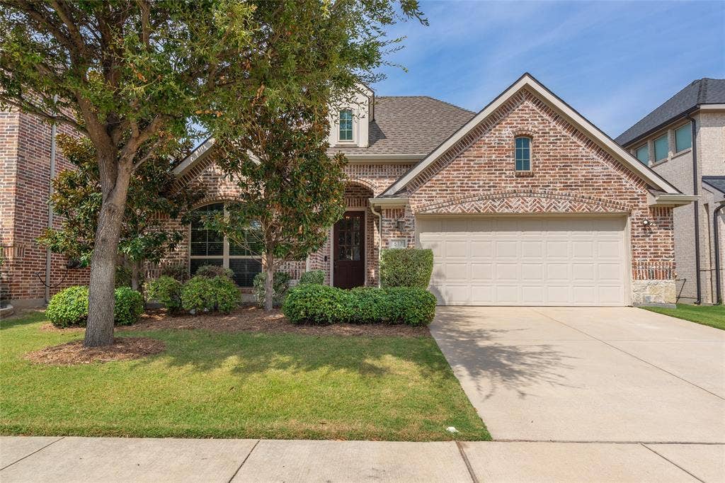 Brick facade with stone accents, a gabled roofline, an attached garage, a concrete driveway, and established front landscaping