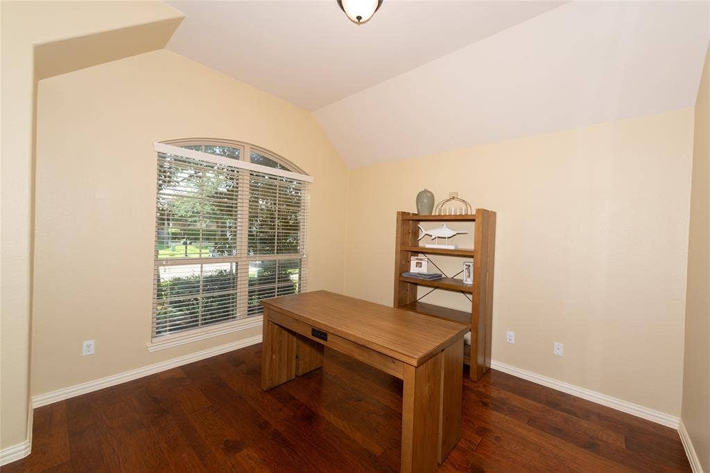 Vaulted ceiling with an arched window and wood-finish flooring