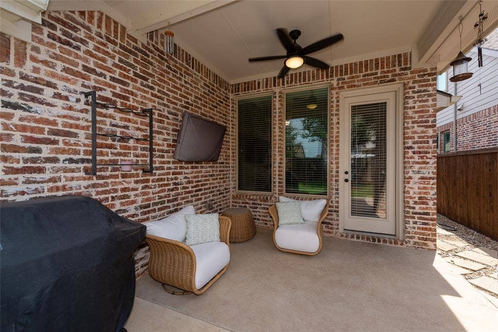 Covered patio featuring a ceiling fan, brick accent wall, and a full-light door with integrated blinds