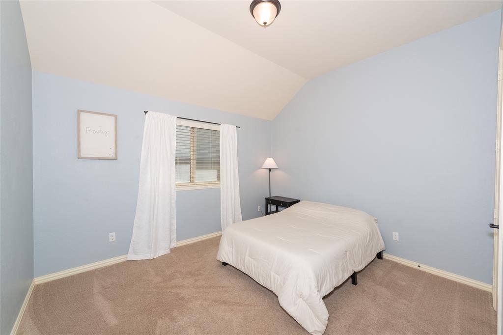 Vaulted ceiling, wall-to-wall carpeting, window with blinds, overhead lighting fixture, and a solid interior door