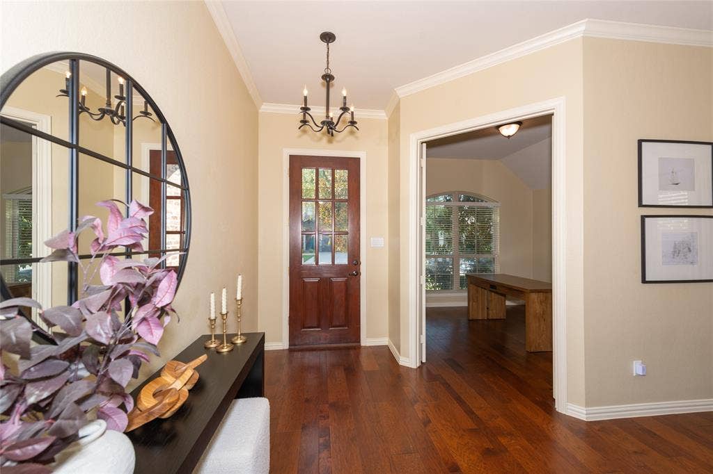 Hardwood flooring, crown molding, a paneled entry door with glass inserts, and a chandelier lighting fixture