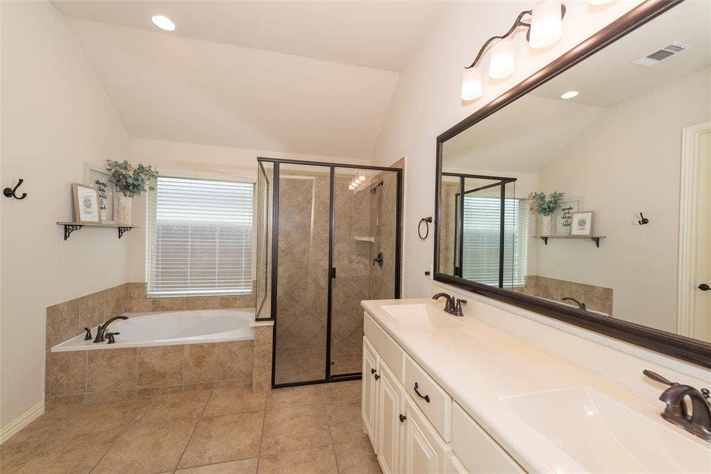Dual vanity with integrated sinks, framed mirror, built-in soaking tub, and enclosed shower with tiled surround