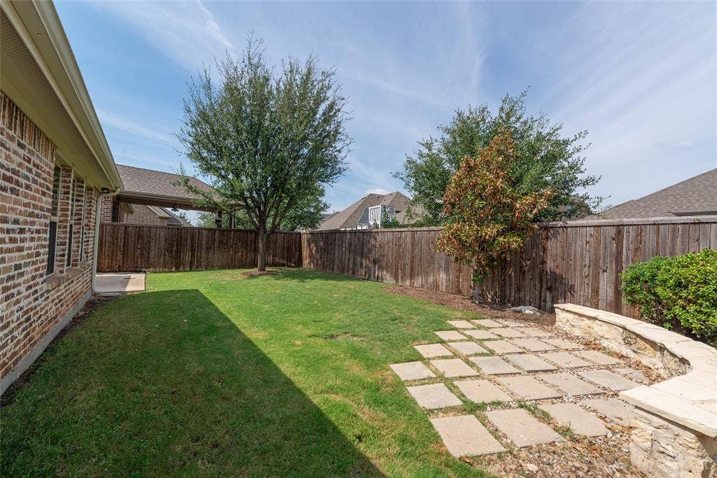 Expansive backyard featuring a manicured lawn, stone paver patio, stone retaining wall, and wood privacy fencing