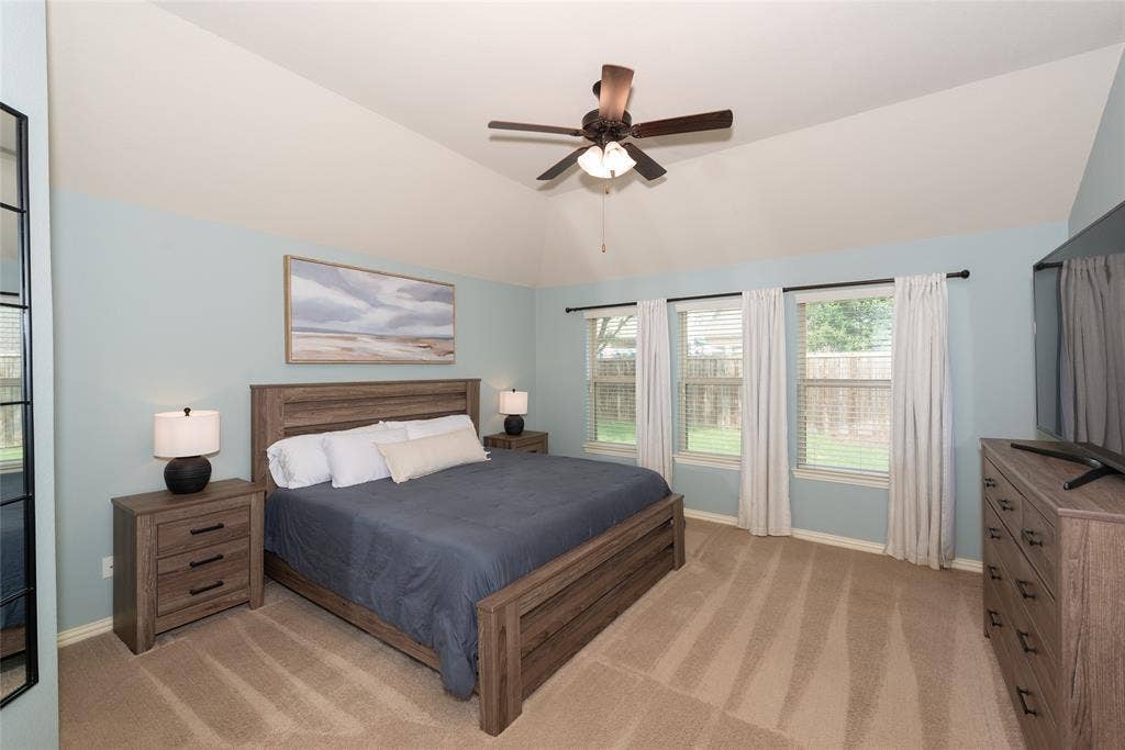 Vaulted ceiling with a ceiling fan, three windows, and carpeted flooring