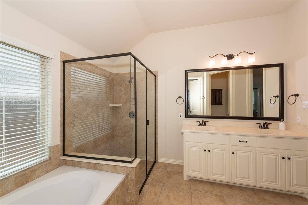 Tile flooring, dual vanity with undermount sinks, separate soaking tub, and enclosed shower with tile surround