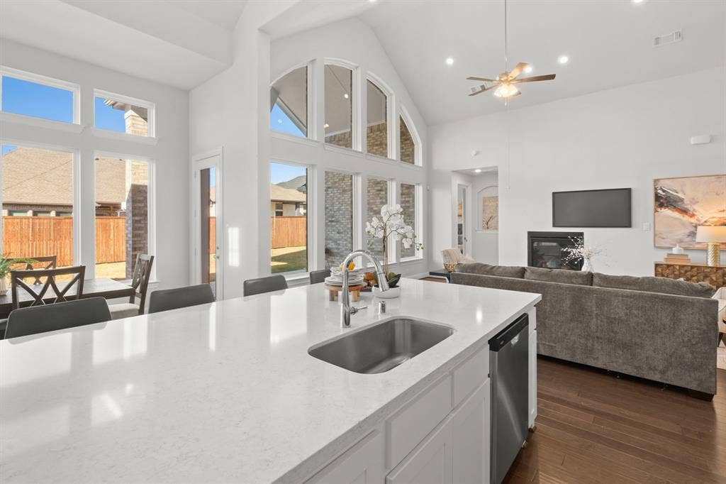 1320 Cartona Road, Fate, TX 75087 Quartz Kitchen island with a stainless steel sink, white cabinetry, and a light-toned countertop over looking the nook dining and living room