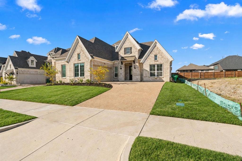 1320 Cartona Road, Fate, TX 75087 Stone exterior with multiple gables, large windows, an expansive driveway, and manicured landscaping
