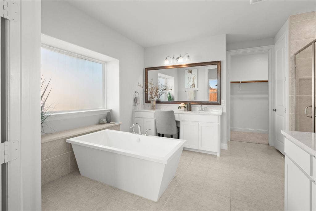 1320 Cartona Road, Fate, TX 75087 Freestanding soaking tub with tiled surround, dual vanity with undermount sinks, frameless glass shower enclosure, and neutral tile flooring