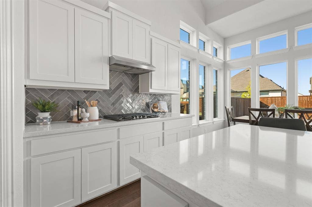 1320 Cartona Road, Fate, TX 75087 White shaker cabinetry with a herringbone tile backsplash and quartz island