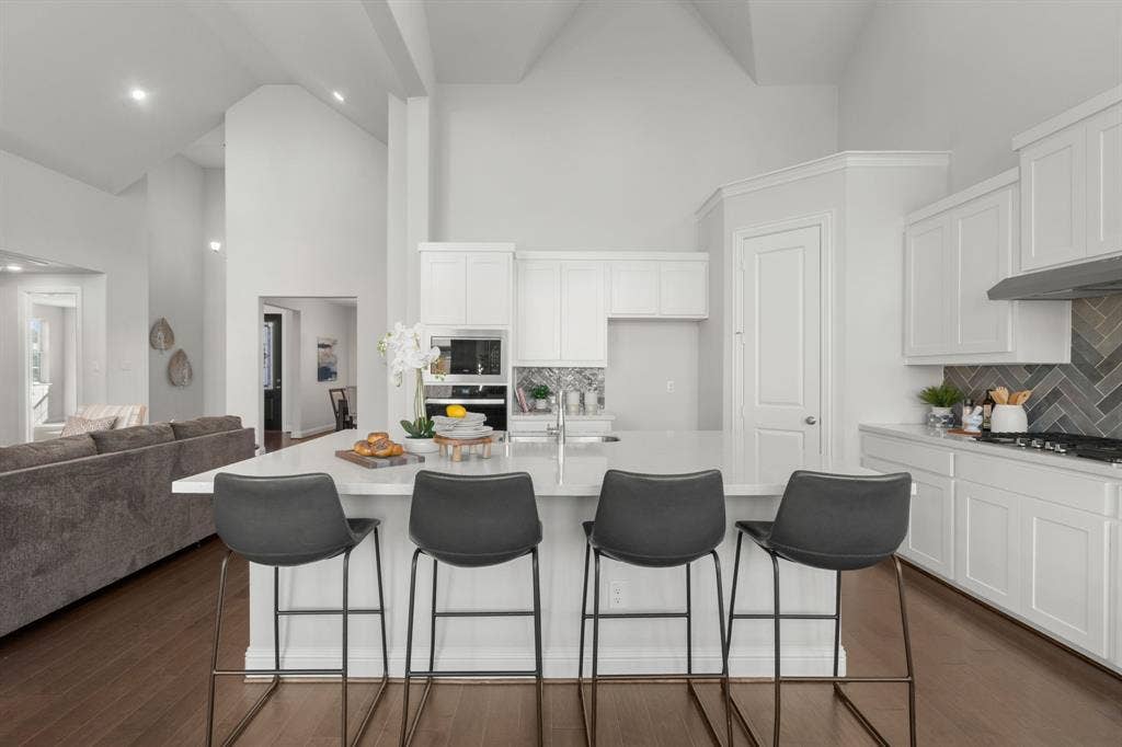 1320 Cartona Road, Fate, TX 75087 White shaker cabinetry, herringbone tile backsplash, stainless steel appliances, central island with seating, and wood-finish flooring