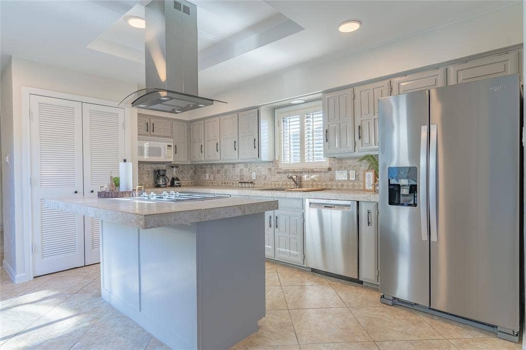 1011 Wimbledon Lane, Plano, TX 75075 Kitchen featuring an island with cooktop, stainless steel appliances, white cabinetry, decorative backsplash, and tiled flooring