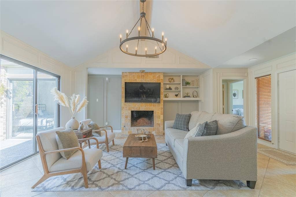 1011 Wimbledon Lane, Plano, TX 75075 Vaulted ceiling with an iron chandelier, stacked stone fireplace, built-in shelving, tile flooring, and sliding glass doors