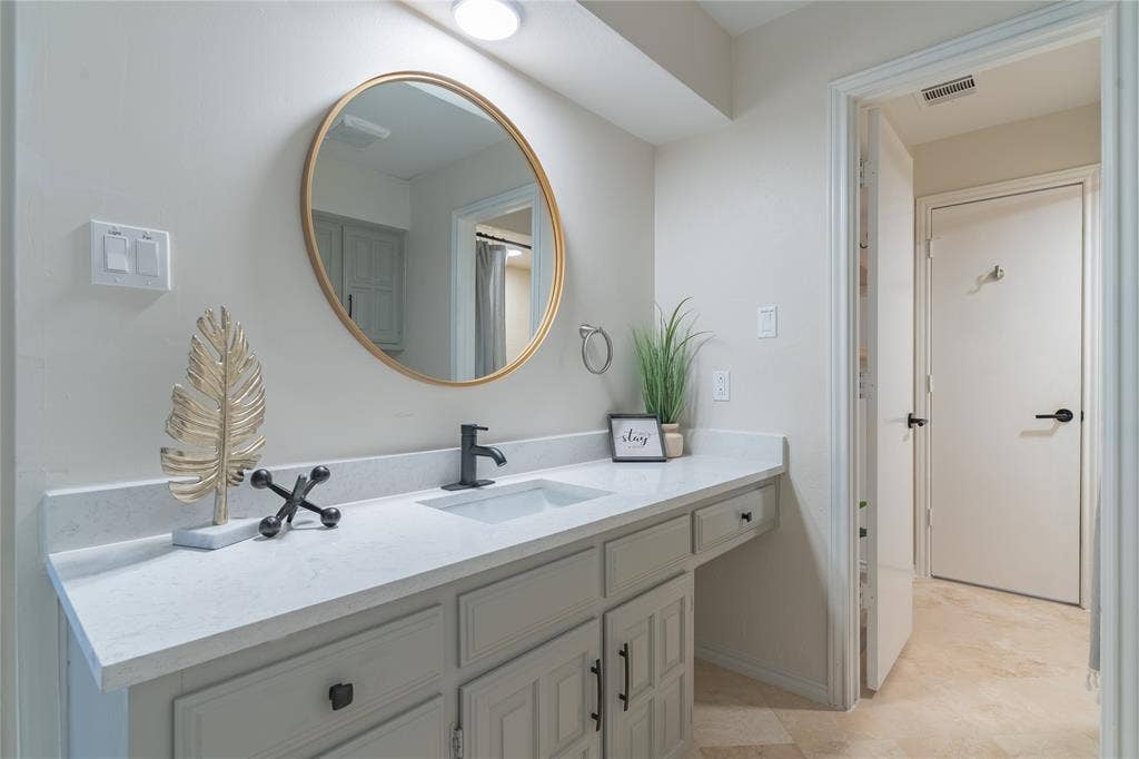 1011 Wimbledon Lane, Plano, TX 75075 Vanity with a gold-framed circular mirror, white countertop, matte black faucet, and light-colored cabinetry