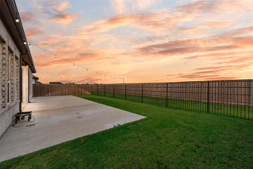 812 Stamford Avenue, Arlington, TX 76002 Expansive concrete patio with string lighting, bordered by a green lawn and a combination wood and metal fence