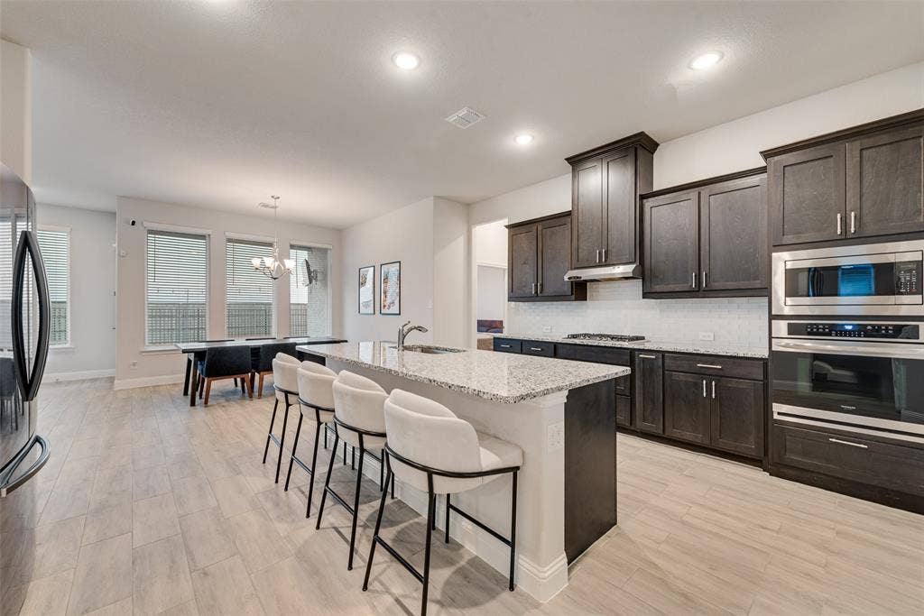 812 Stamford Avenue, Arlington, TX 76002 Open concept kitchen with wood-finish flooring, dark wood cabinetry, stainless steel appliances, a center island with a light-colored countertop, and recessed lighting