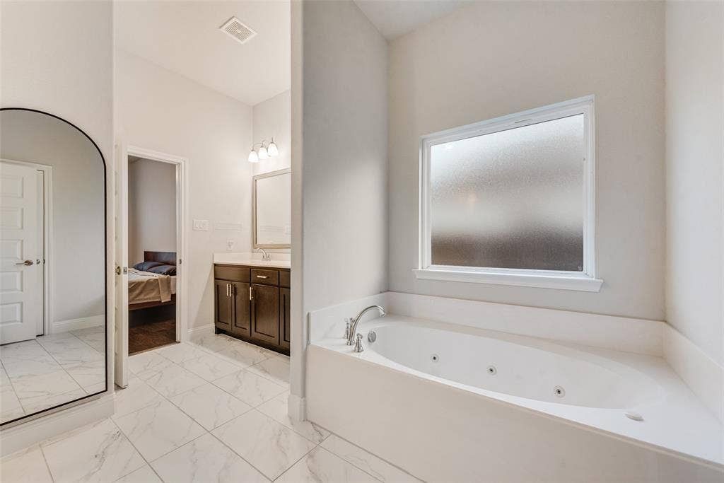 812 Stamford Avenue, Arlington, TX 76002 Soaking tub with jets, white tile flooring, dark wood vanity, integrated sink, and wall-mounted light fixture