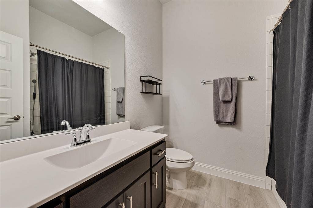 812 Stamford Avenue, Arlington, TX 76002 Bathroom featuring a dark wood-finish vanity with a white countertop and integrated sink, a large wall-mounted mirror, light-toned wood-finish flooring, and a shower with white subway tile