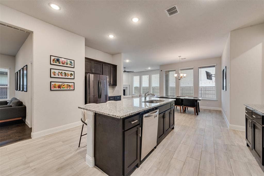 812 Stamford Avenue, Arlington, TX 76002 Expansive kitchen island with a granite countertop and integrated sink, dark wood cabinetry, stainless steel dishwasher, and recessed lighting