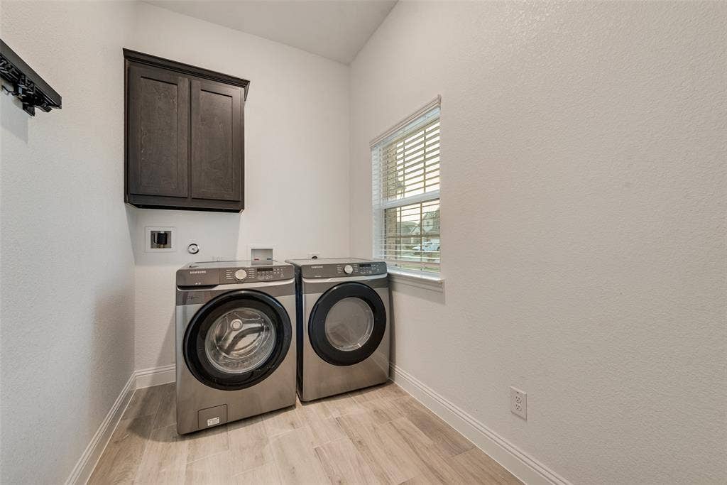812 Stamford Avenue, Arlington, TX 76002 Laundry room featuring wood-finish flooring, a built-in dark wood-tone cabinet, and a window with blinds