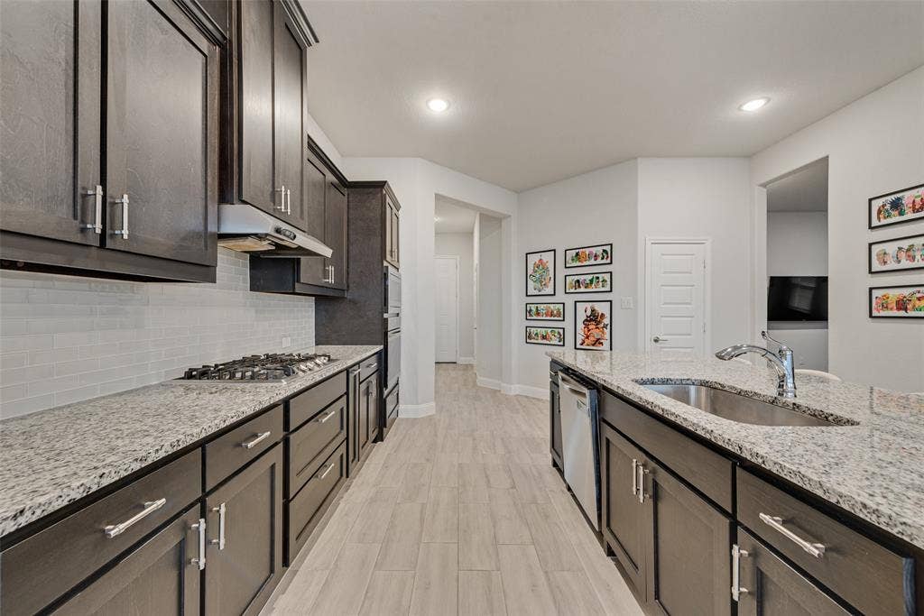 812 Stamford Avenue, Arlington, TX 76002 Kitchen featuring dark wood-finish cabinetry, light-toned countertops, a built-in gas range with a vent hood, a stainless steel sink, and wood-finish flooring