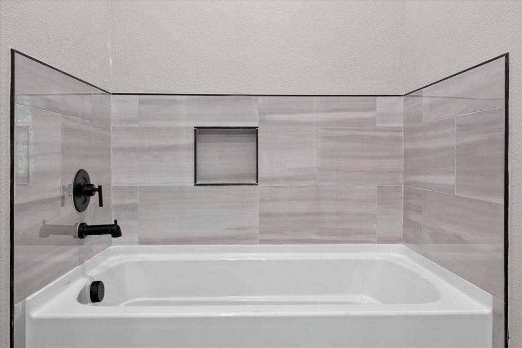 7919 N kiska Street, Dallas, TX 75216 Bathtub with light-toned rectangular wall tiling, matte black fixtures, and a recessed shower niche