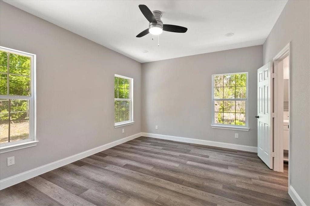 7919 N kiska Street, Dallas, TX 75216 Spacious room featuring wood-finish flooring, two windows with white trim, and a ceiling fan with integrated lighting