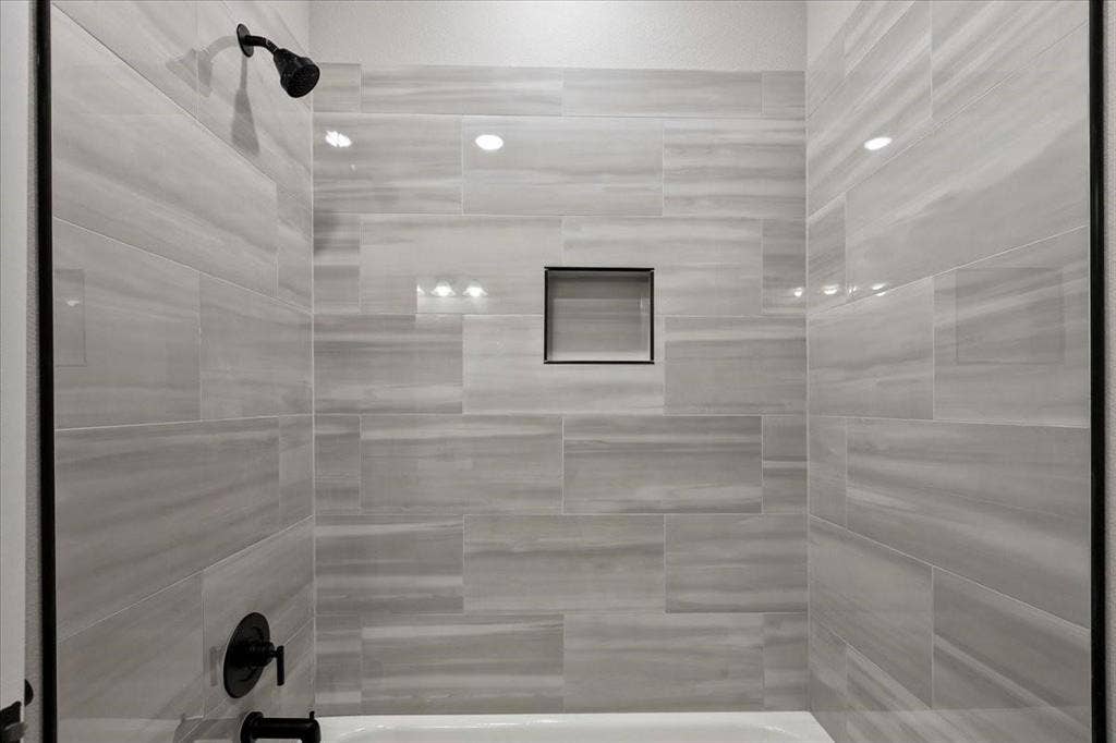 7919 N kiska Street, Dallas, TX 75216 Bathtub with matte black fixtures, recessed shower niche, and light-toned horizontal tile surround