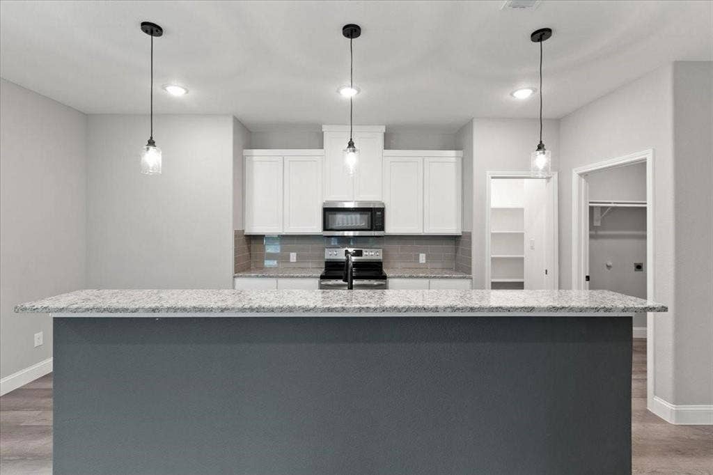 7919 N kiska Street, Dallas, TX 75216 Kitchen featuring a gray island with a light-toned countertop, white cabinetry, a tile backsplash, and stainless steel appliances
