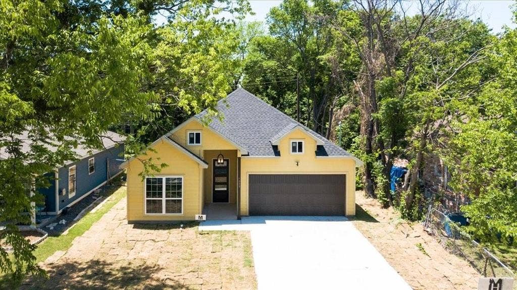 7919 N kiska Street, Dallas, TX 75216 Single-story residence featuring a gray shingle roof, yellow exterior siding, a two-car garage, and a concrete driveway