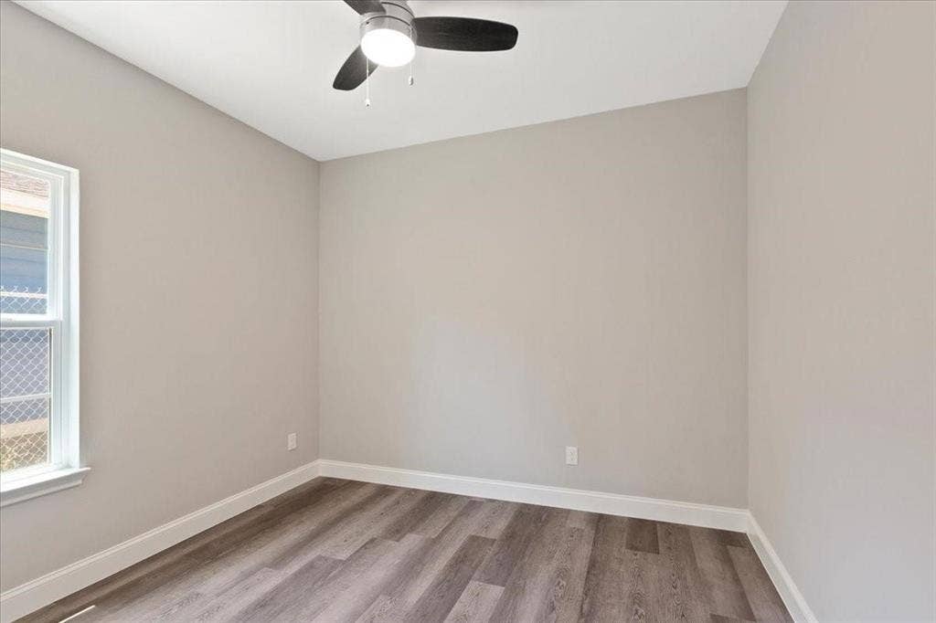7919 N kiska Street, Dallas, TX 75216 Light-filled room featuring wood-finish flooring, neutral wall paint, white trim, a single window, and a ceiling fan with integrated lighting