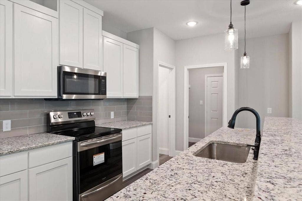7919 N kiska Street, Dallas, TX 75216 Kitchen with white shaker cabinetry, stainless steel appliances, speckled countertops, and a subway tile backsplash