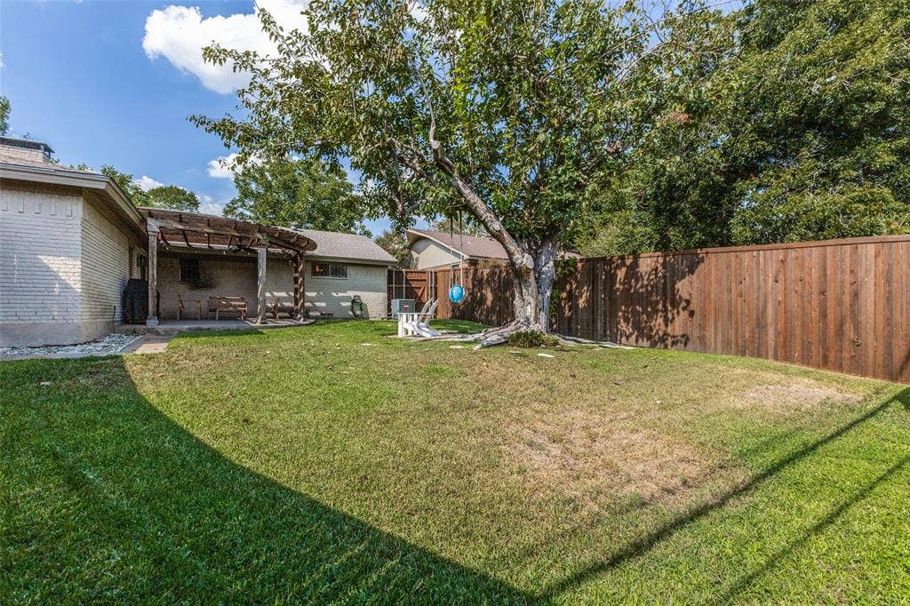 9864 Shoreview Road, Dallas, TX 75238 Expansive backyard with a manicured lawn, established tree, and a solid wood fence
