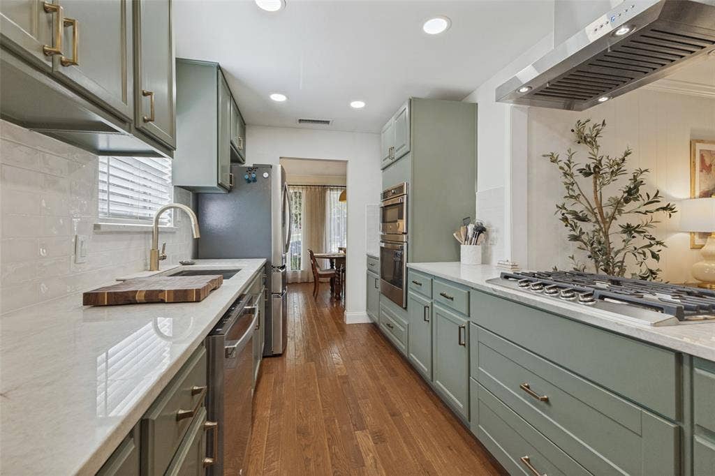 9864 Shoreview Road, Dallas, TX 75238 Galley kitchen featuring light green cabinetry, integrated stainless steel appliances, a gas range with a stainless steel vent hood, and wood-finish flooring