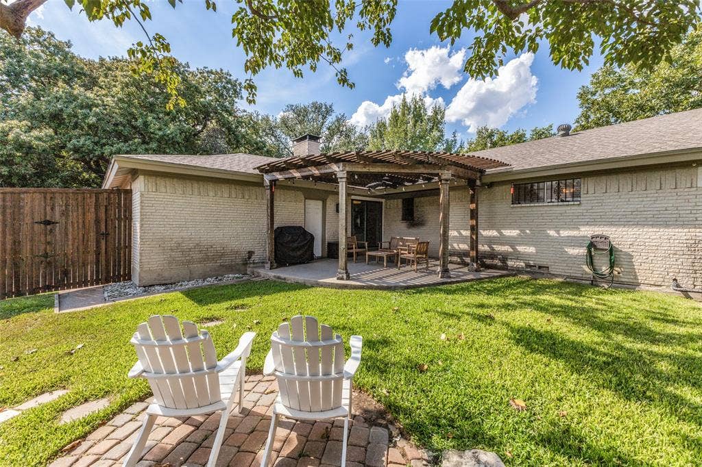 9864 Shoreview Road, Dallas, TX 75238 Expansive backyard featuring a manicured lawn, brick paver patio, wood pergola, and full privacy fencing