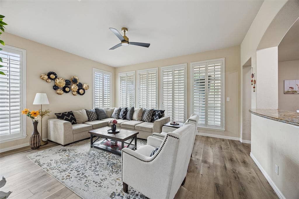 2865 Ridge View Road, Frisco, TX 75034 Spacious living area featuring wood-finish flooring, multiple windows with white plantation shutters, a ceiling fan, and an arched entryway