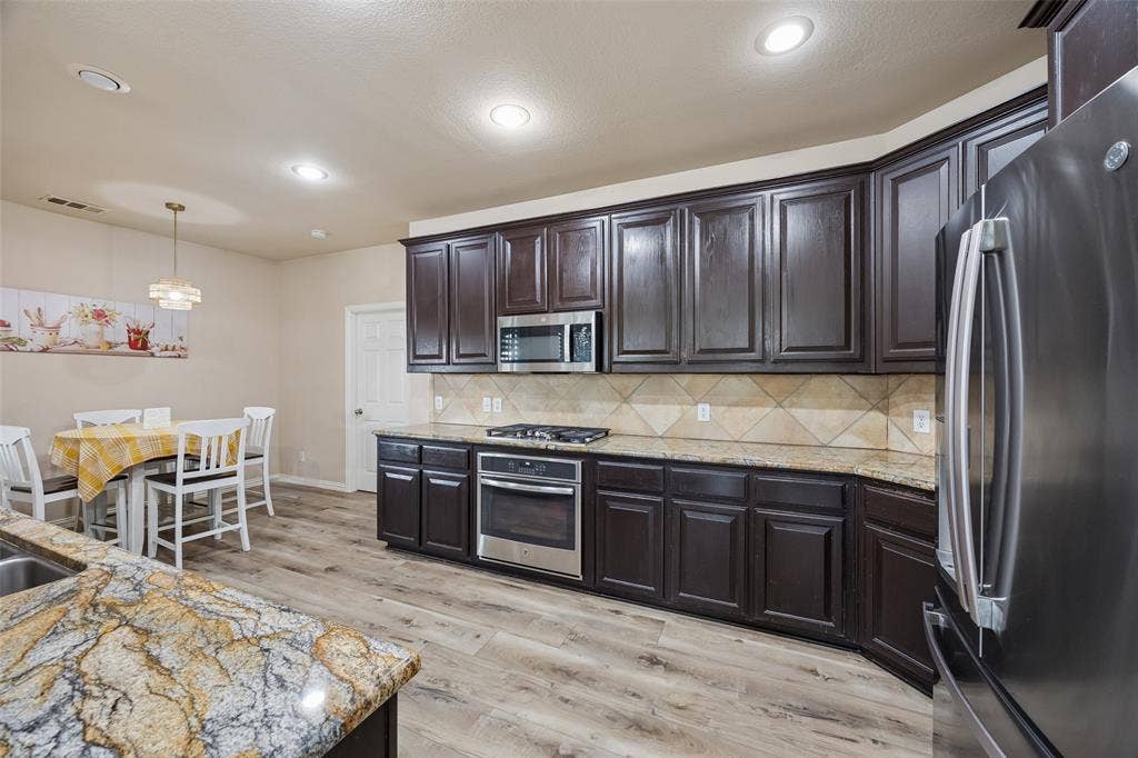 2865 Ridge View Road, Frisco, TX 75034 Kitchen featuring dark wood cabinetry, light-toned countertops, a diagonal tile backsplash, stainless steel appliances, and wood-finish flooring