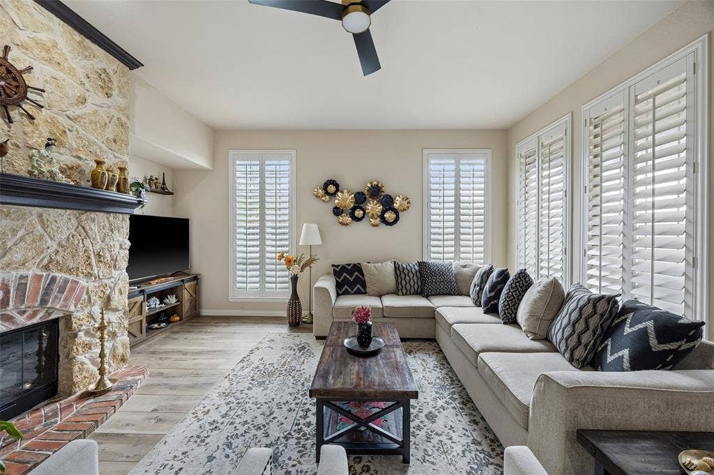 2865 Ridge View Road, Frisco, TX 75034 Stone-clad fireplace with brick hearth, wood-finish flooring, plantation shutters, and a ceiling fan