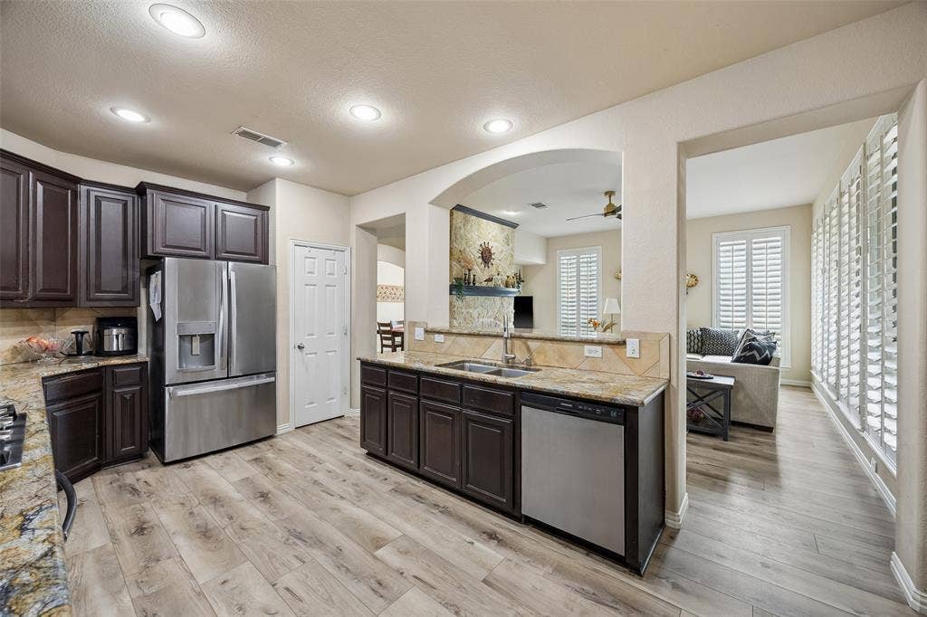 2865 Ridge View Road, Frisco, TX 75034 Kitchen featuring wood-finish flooring, dark wood cabinetry, stainless steel appliances, and stone countertops with a tile backsplash
