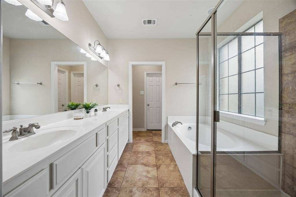 2865 Ridge View Road, Frisco, TX 75034 Dual vanity with white cabinetry and integrated sinks, large wall-mounted mirror, separate soaking tub, and a glass-enclosed shower with tiled surround